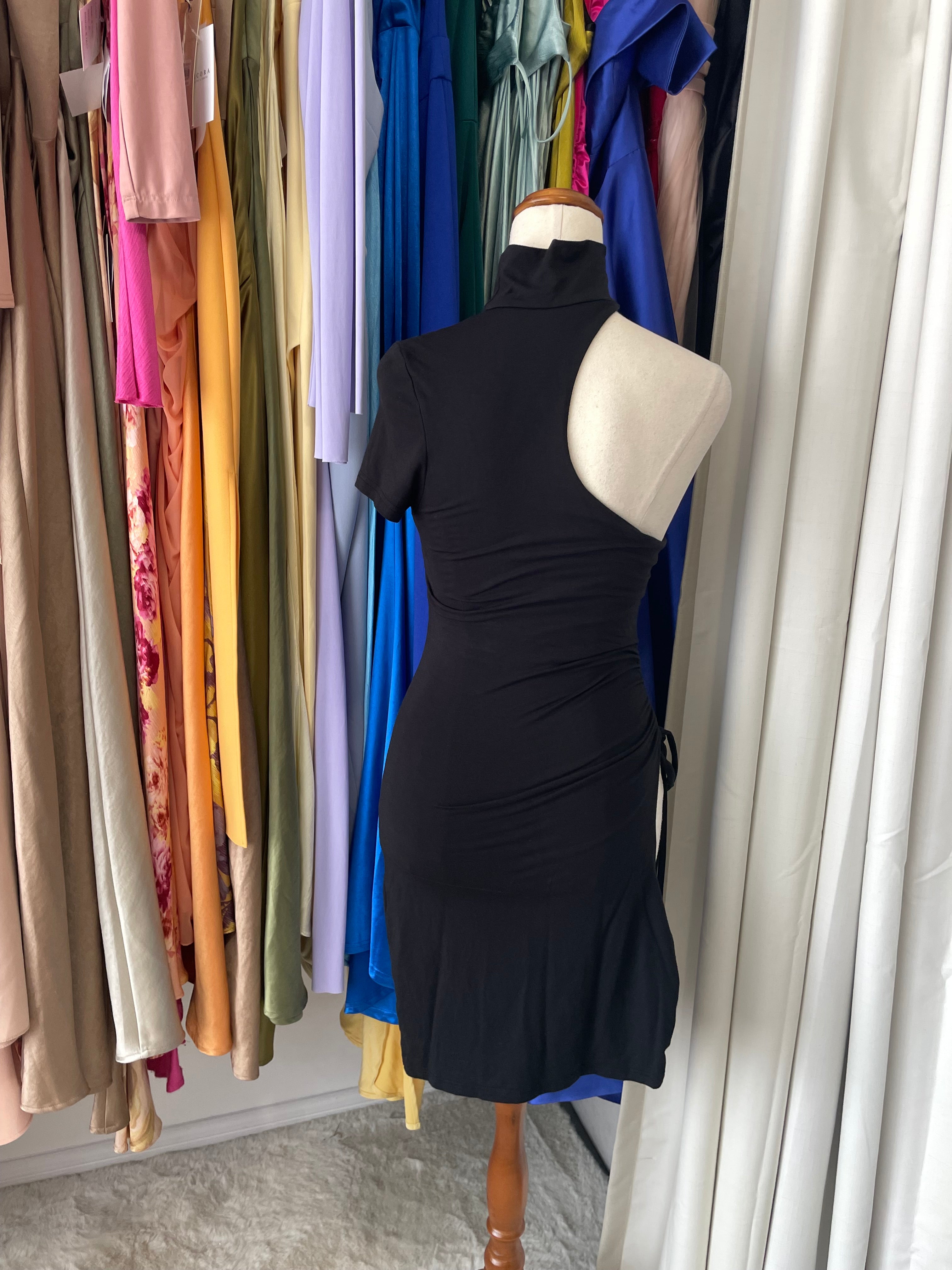 Mannequin wearing a black dress with a white collar on a stack of colorful fabrics.