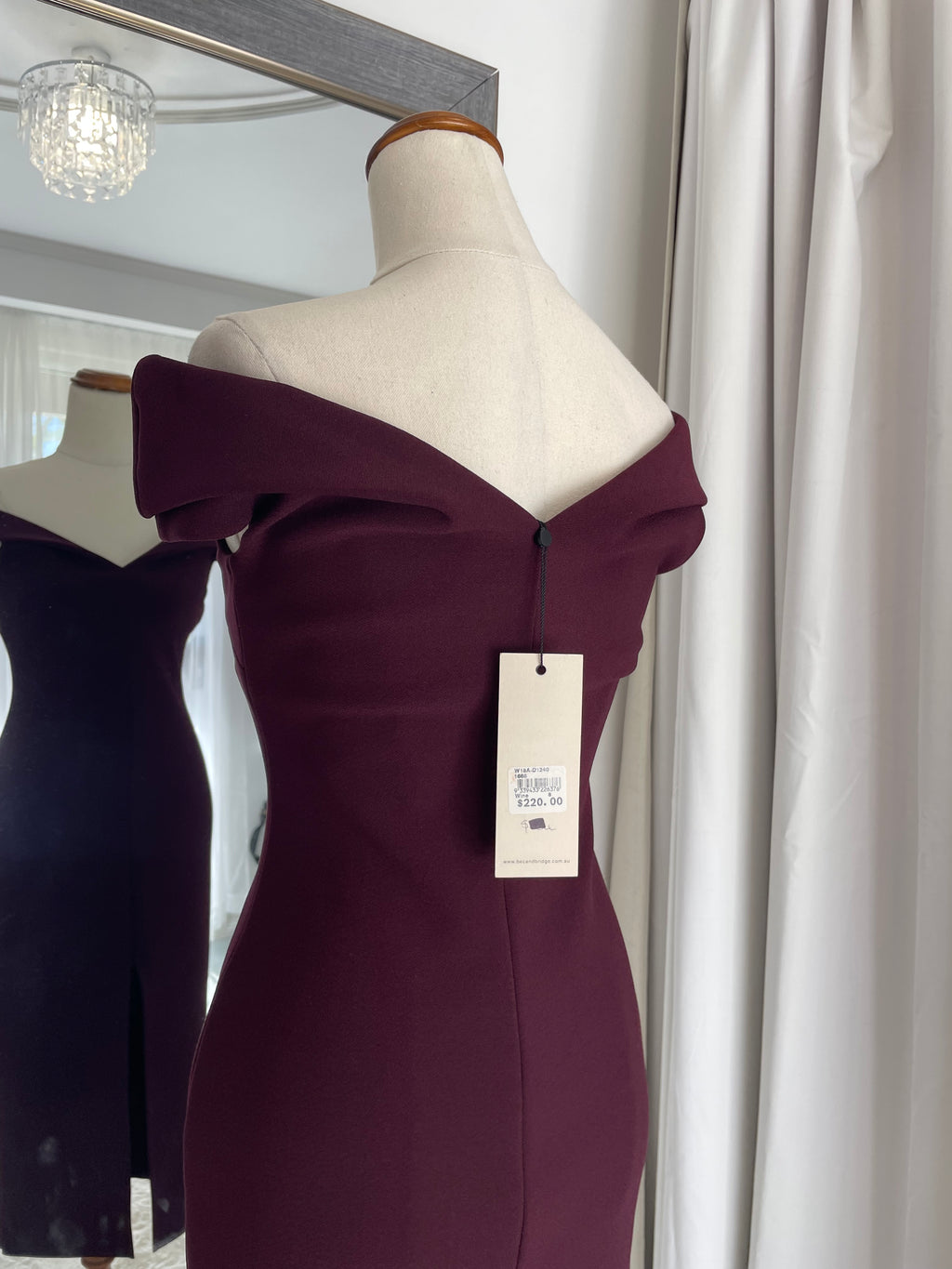 Burgundy dress on a mannequin with a tag in a store setting.