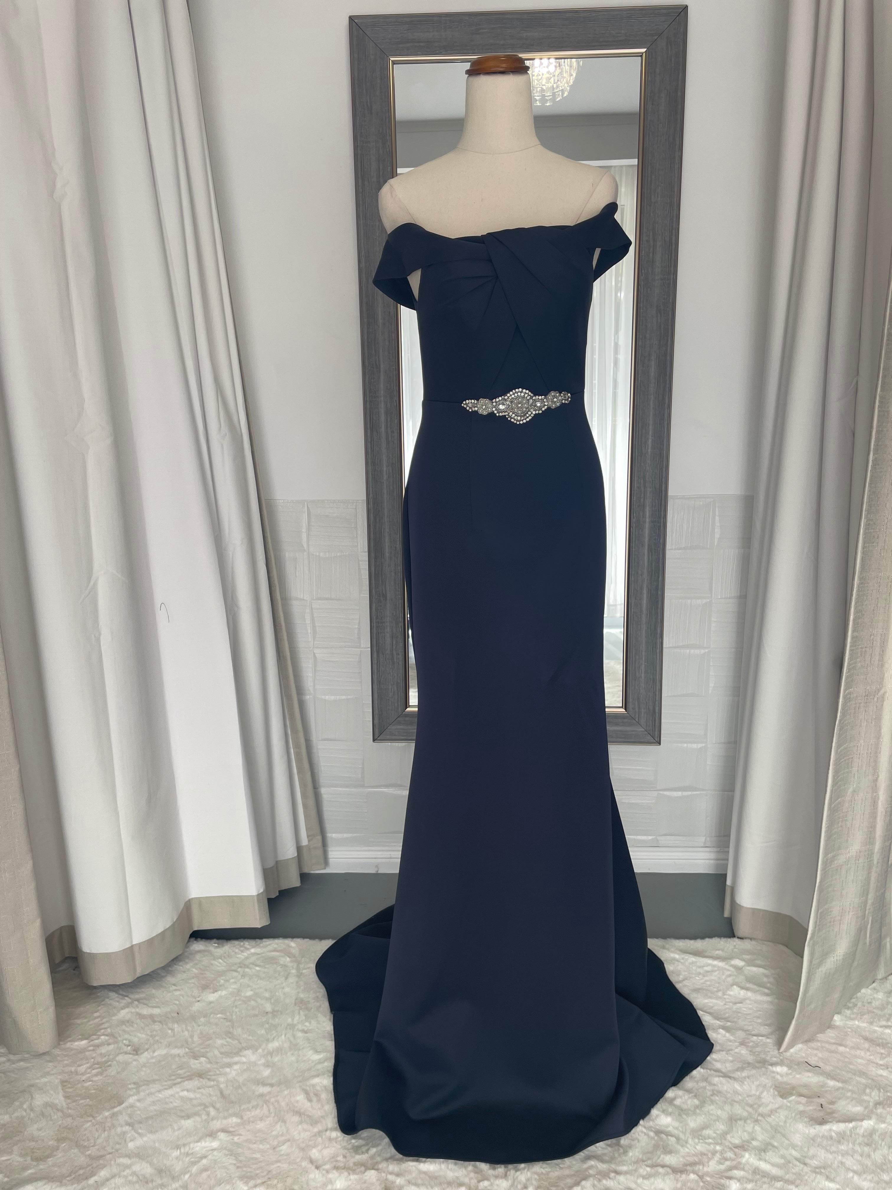 Front of Navy lue off the shoulder formal gown. twist front knot detail. long train and finger loop. crystal waist applique. 