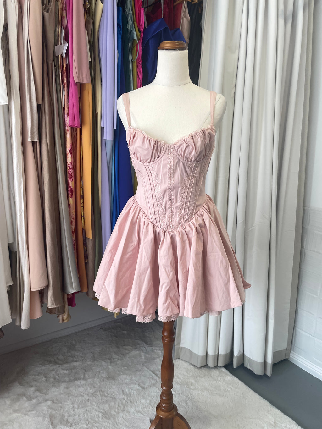 Baby Boo Josie is an elegantly crafted corset dress featuring delicate lace detailing, structured boning for a refined silhouette, and a graceful full skirt. The blush tone and tie bow back create a romantic aesthetic, while underwired cups and full lining ensure comfort and support.