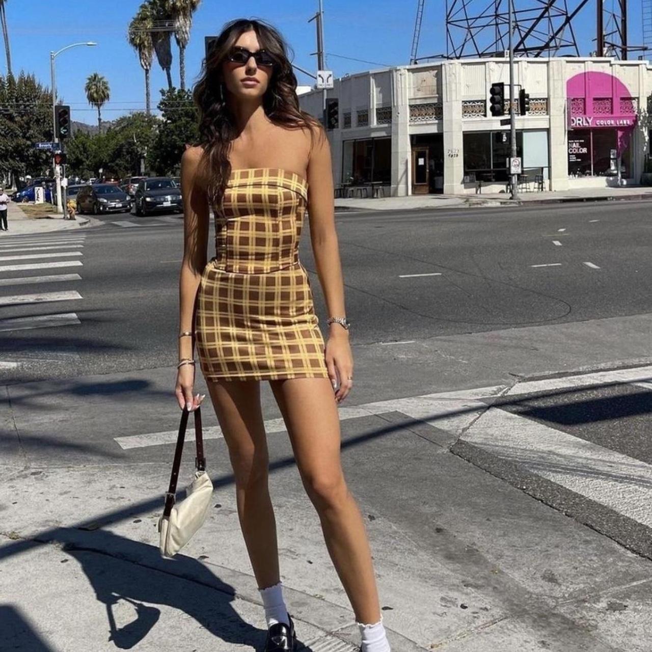 Woman in a checkered dress standing on a city street corner.