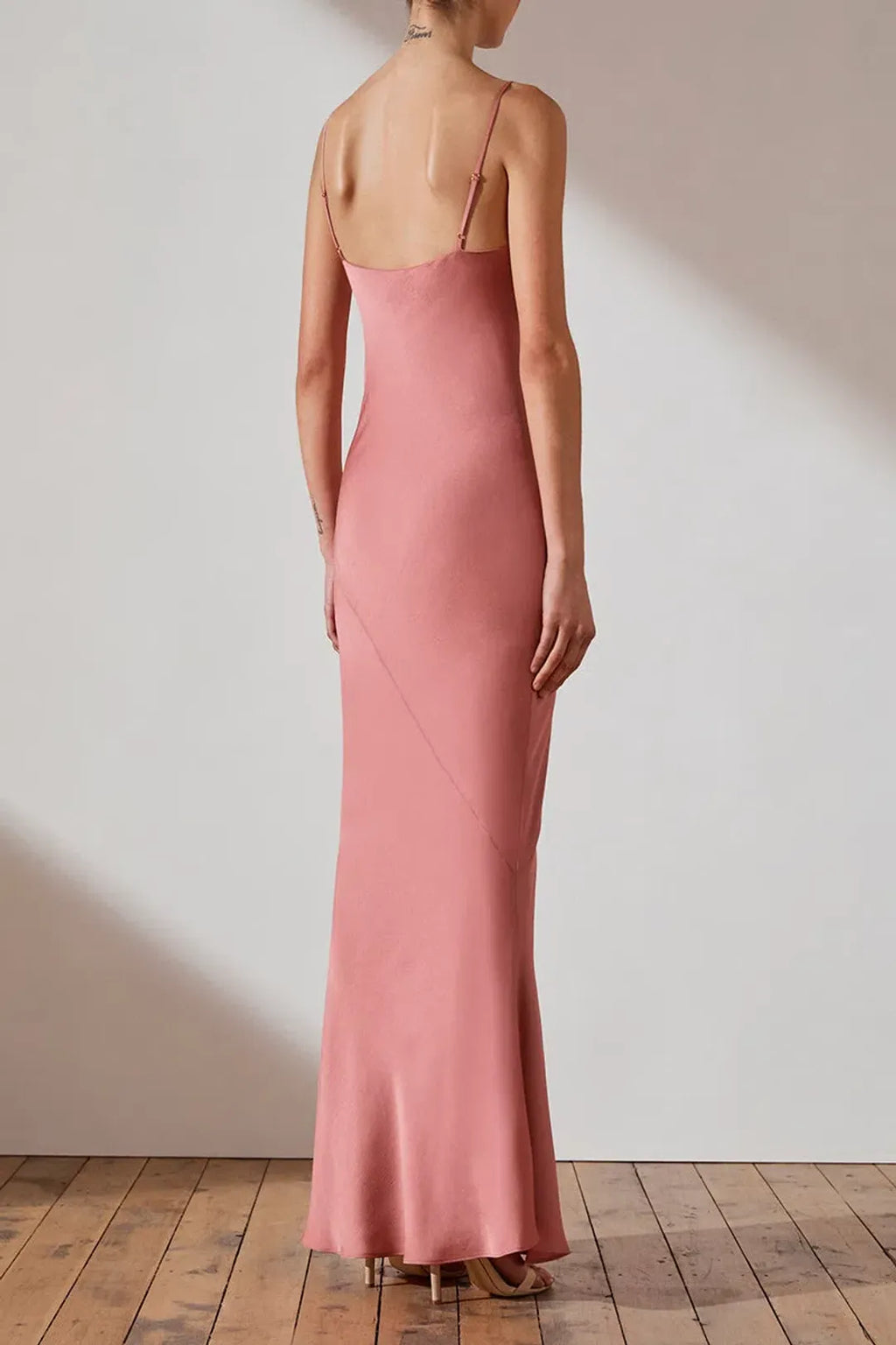 Woman wearing a pink slip dress standing against a plain wall.