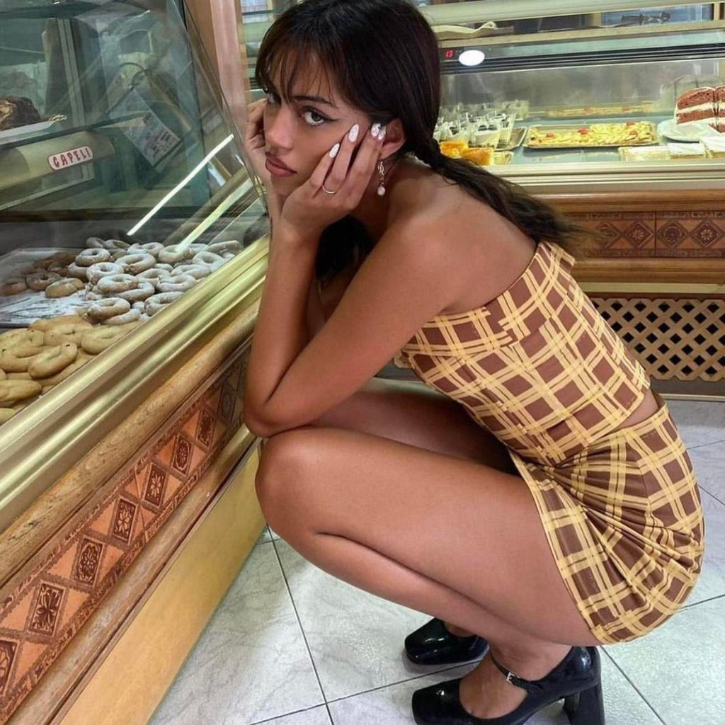 Woman in a checkered dress posing in front of a bakery display case.