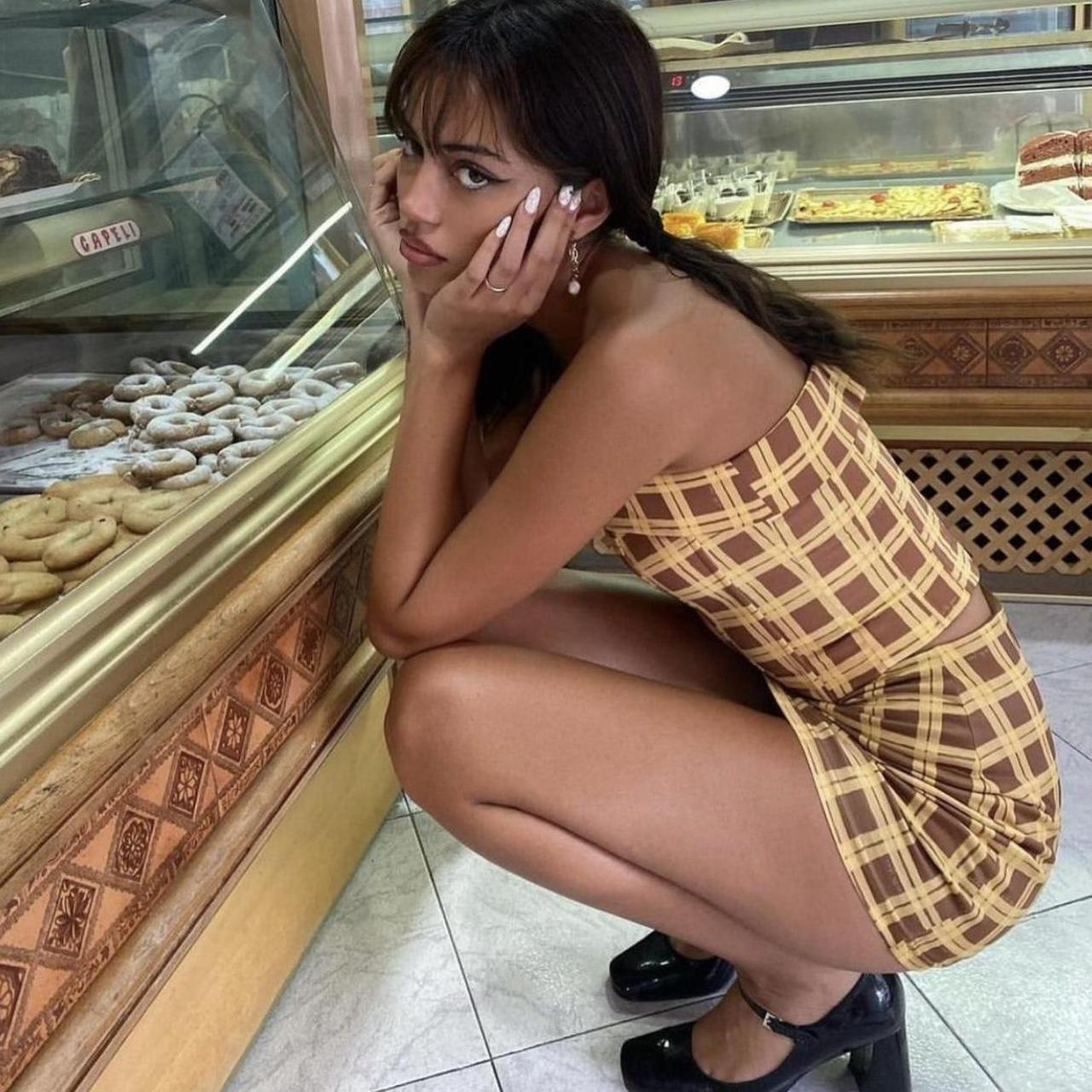Woman in a checkered dress posing in front of a bakery display case.