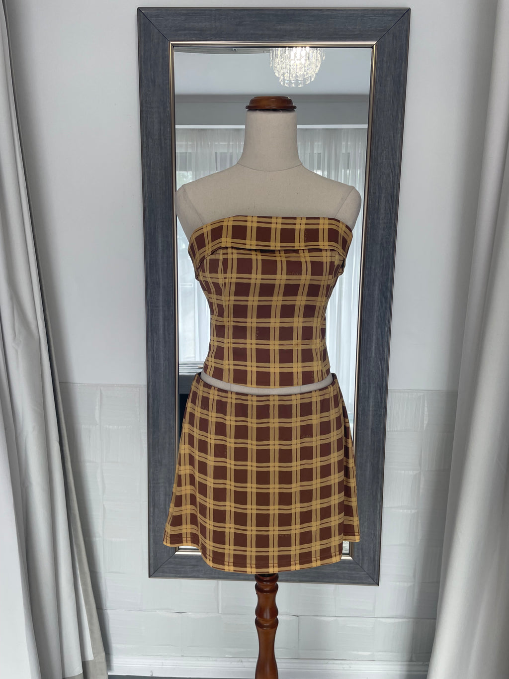 Mannequin wearing a plaid dress in front of a large mirror with a gray frame.