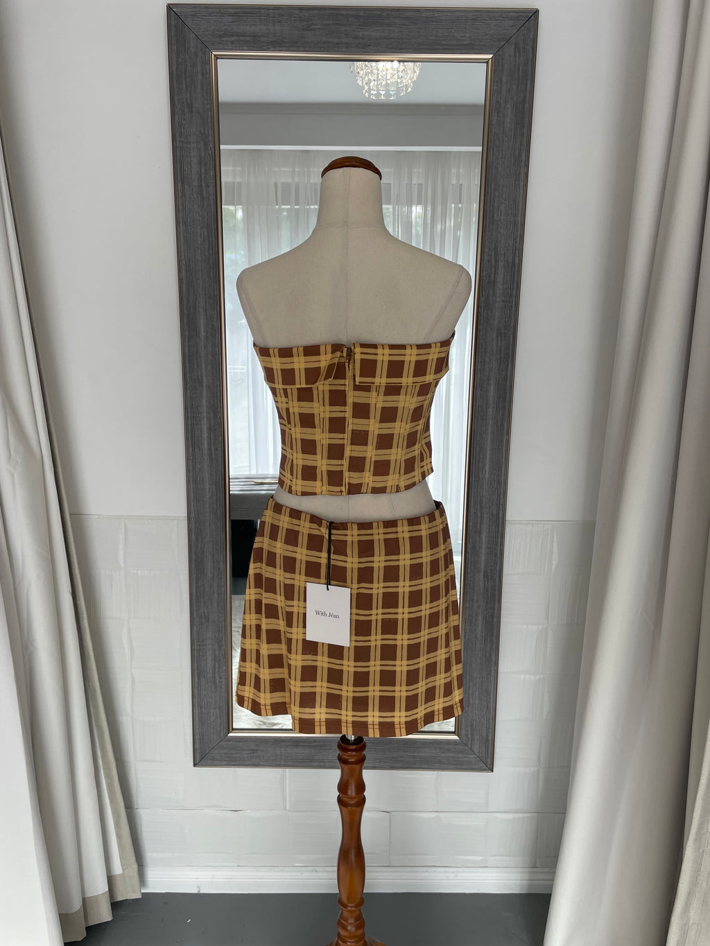 Mannequin with plaid shirt inside a framed mirror on a white wall.