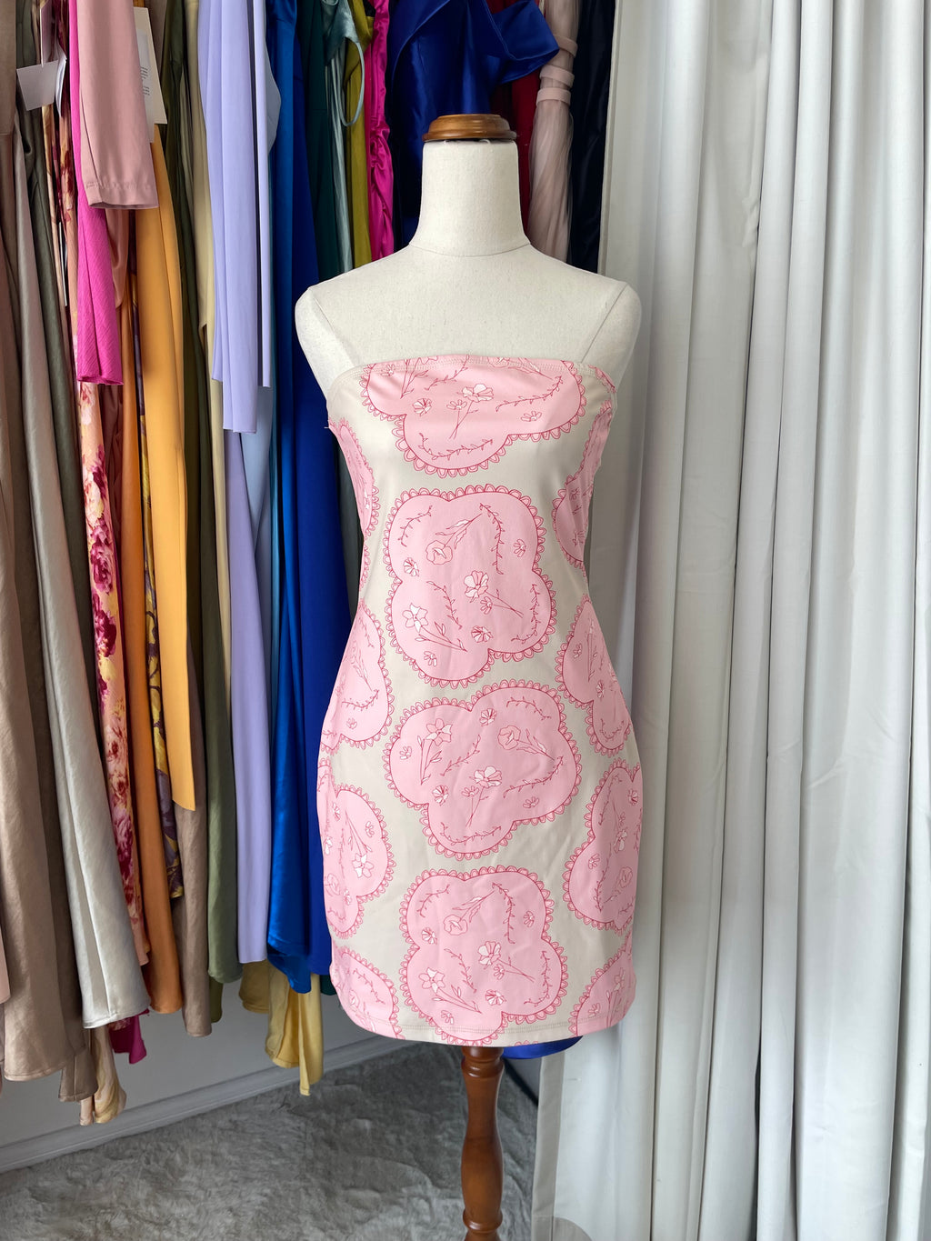 Mannequin with pink floral dress in front of hanging clothes 
