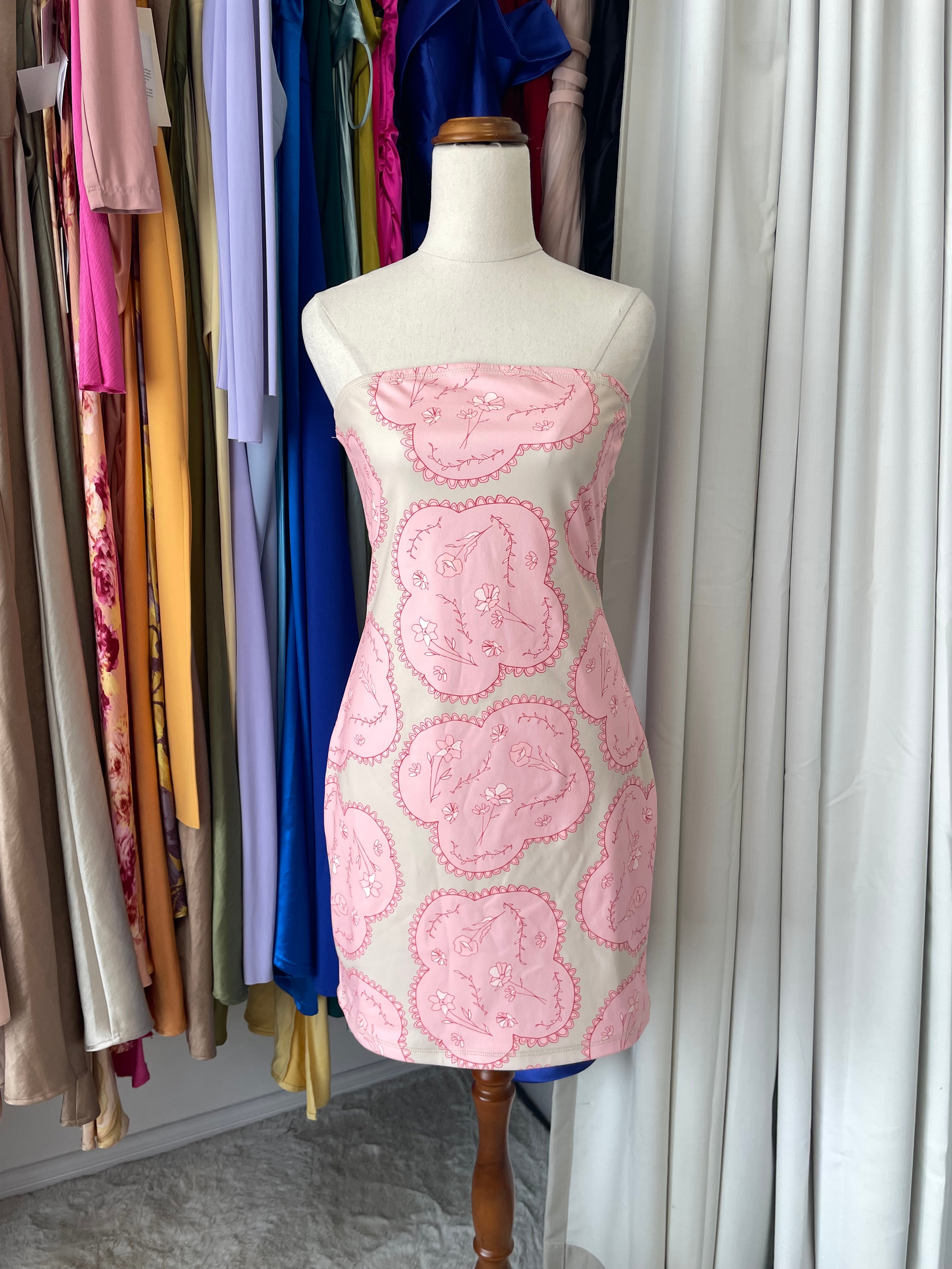 Mannequin with pink floral dress in front of hanging clothes 
