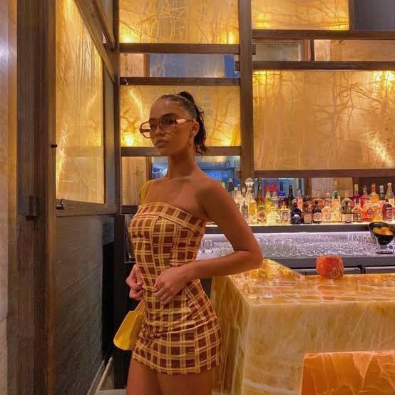 Woman in a checkered dress standing in a bar with a gold interior.