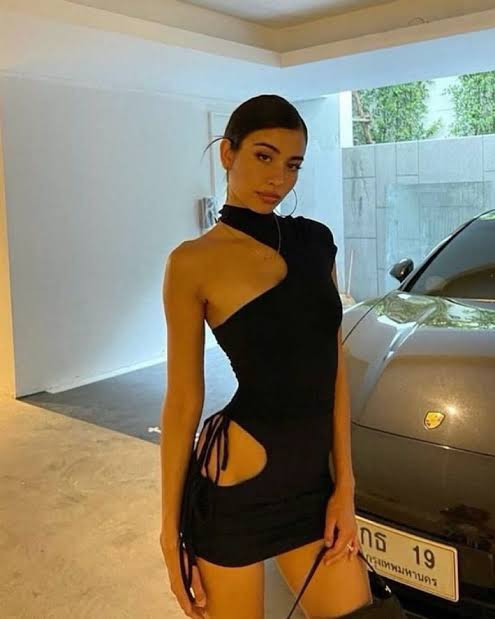 Woman in a black dress standing next to a car with a visible logo.