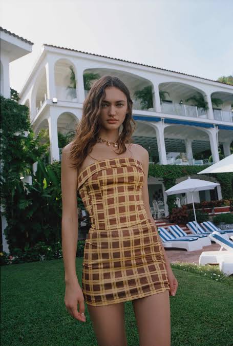Woman in a checkered dress standing in front of a resort building with a pool area.